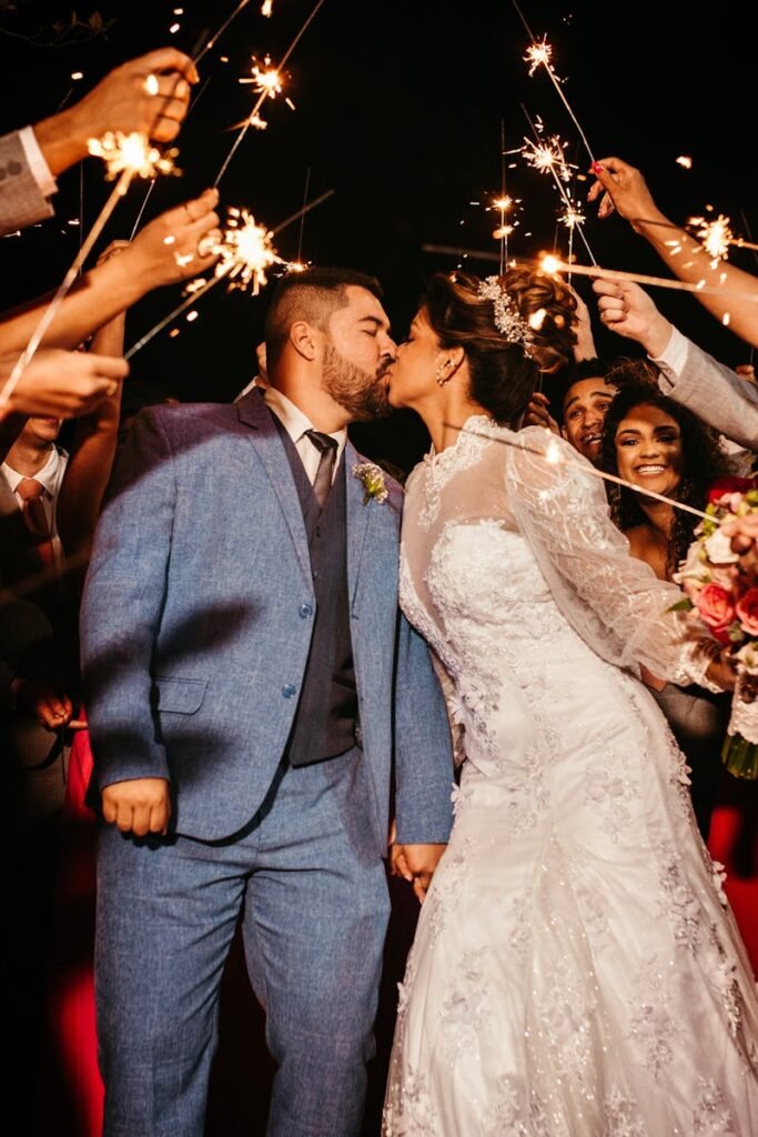 Bride and groom kissing amid sparklers during wedding celebration surrounded by guests.
